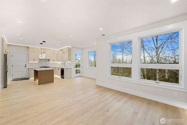 unfurnished living room featuring light wood finished floors, a sink, baseboards, recessed lighting, and visible vents