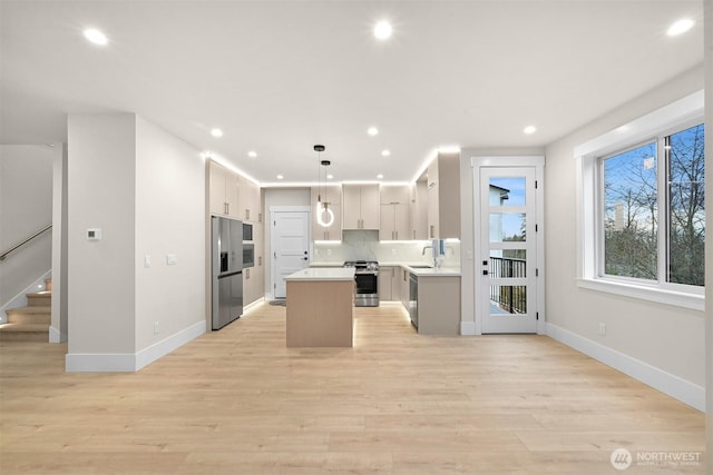 kitchen featuring stainless steel appliances, a sink, baseboards, light countertops, and a kitchen island
