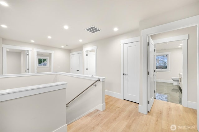hallway with an upstairs landing, light wood finished floors, baseboards, visible vents, and recessed lighting