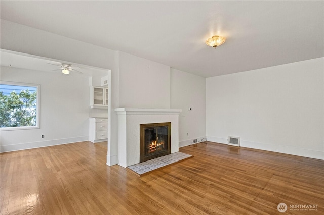 unfurnished living room featuring visible vents, wood finished floors, baseboards, a tile fireplace, and a ceiling fan