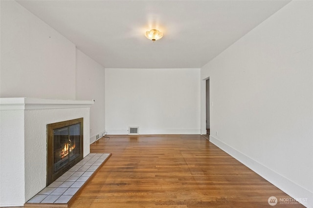 unfurnished living room featuring a tiled fireplace, wood finished floors, and visible vents