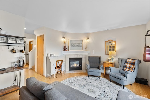 living area featuring a tiled fireplace, light wood-type flooring, and stairs