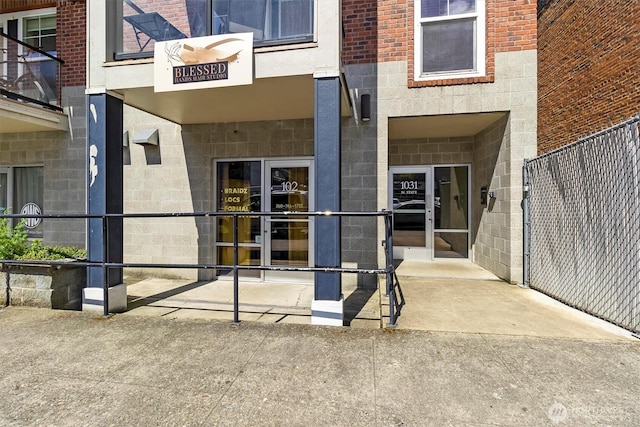 view of exterior entry with fence, concrete block siding, and brick siding