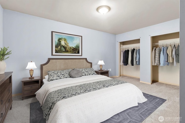 bedroom featuring baseboards, two closets, and light carpet