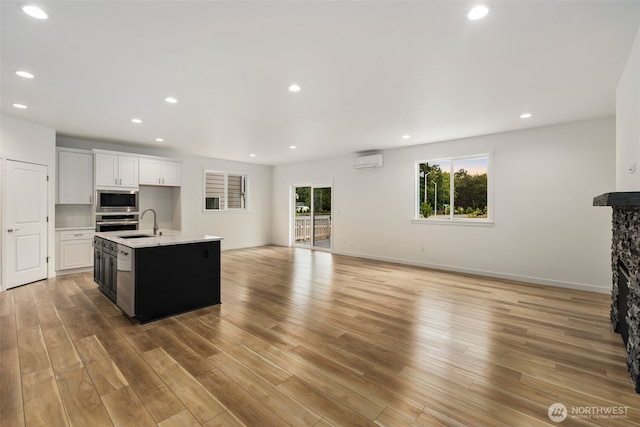 kitchen with appliances with stainless steel finishes, light countertops, a wall mounted AC, a sink, and open floor plan