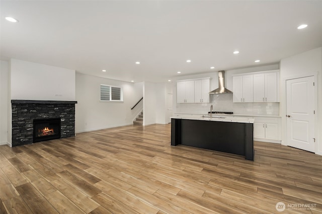 kitchen featuring white cabinetry, light wood-style floors, light countertops, open floor plan, and wall chimney exhaust hood