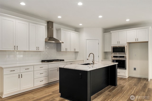 kitchen with wood finished floors, stainless steel appliances, wall chimney range hood, white cabinets, and a sink