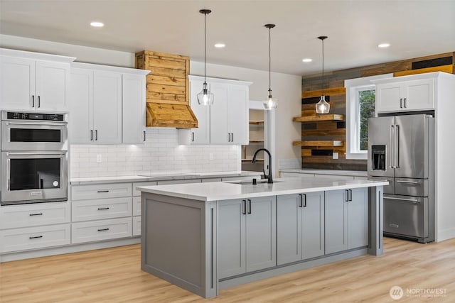 kitchen featuring light wood-style flooring, a sink, tasteful backsplash, light countertops, and appliances with stainless steel finishes
