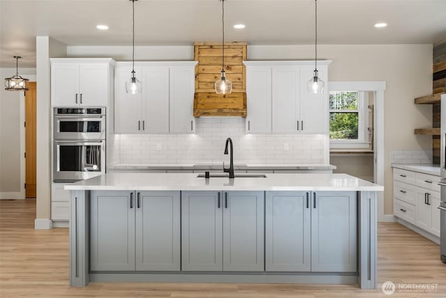kitchen with white cabinets, a sink, backsplash, stainless steel double oven, and light countertops