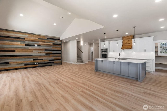 kitchen featuring white cabinets, light wood finished floors, a sink, light countertops, and premium range hood