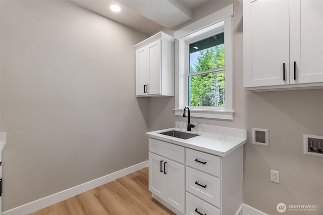 laundry area featuring light wood finished floors, a sink, hookup for a washing machine, baseboards, and cabinet space