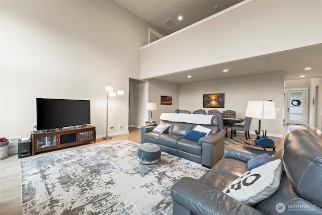 living area with visible vents, baseboards, a high ceiling, recessed lighting, and light wood-style flooring