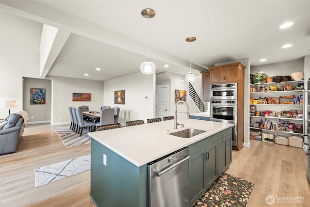 kitchen with a kitchen island with sink, appliances with stainless steel finishes, a sink, open floor plan, and light wood-style floors