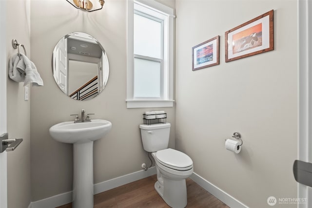 bathroom with baseboards, plenty of natural light, toilet, and wood finished floors