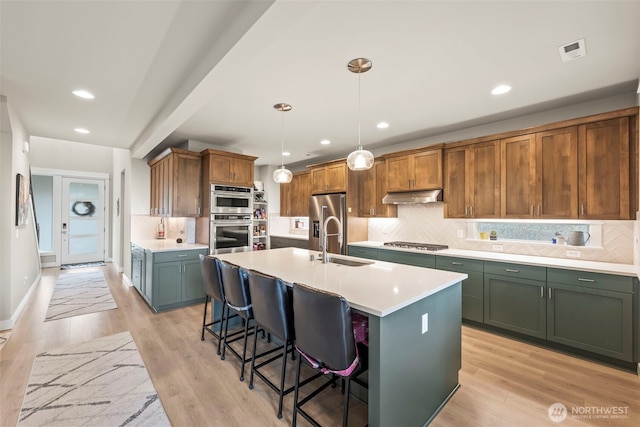 kitchen with a kitchen bar, light countertops, under cabinet range hood, tasteful backsplash, and stainless steel appliances