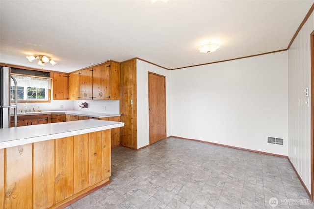 kitchen featuring brown cabinetry, light countertops, a sink, baseboards, and visible vents