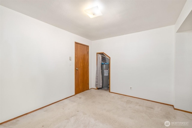 unfurnished room with baseboards, water heater, and carpet