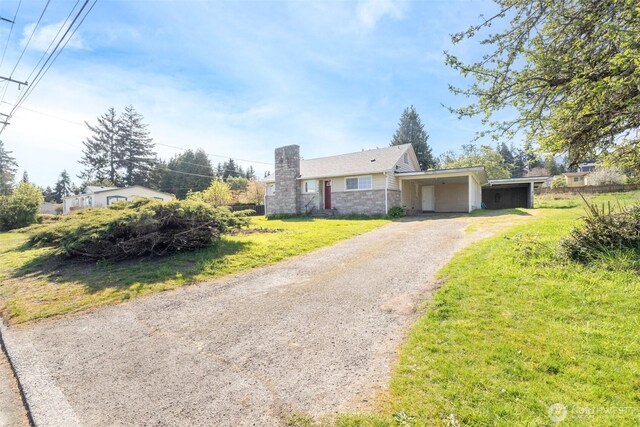 view of front of home featuring a carport, stone siding, a chimney, gravel driveway, and a front lawn