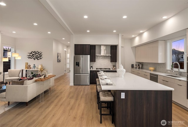 kitchen with modern cabinets, a sink, stainless steel appliances, tasteful backsplash, and wall chimney range hood