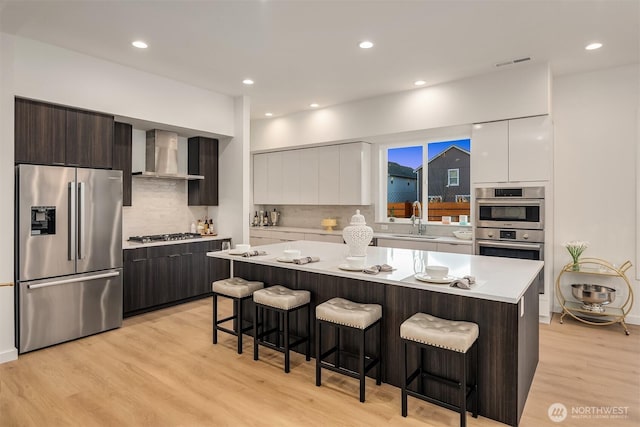 kitchen featuring appliances with stainless steel finishes, wall chimney range hood, a sink, visible vents, and modern cabinets