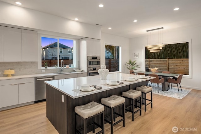 kitchen with a sink, modern cabinets, stainless steel appliances, a kitchen breakfast bar, and white cabinets