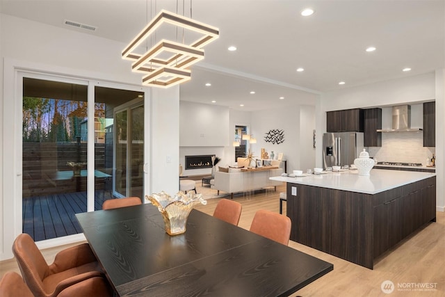 dining area with visible vents, recessed lighting, light wood-style flooring, and a warm lit fireplace