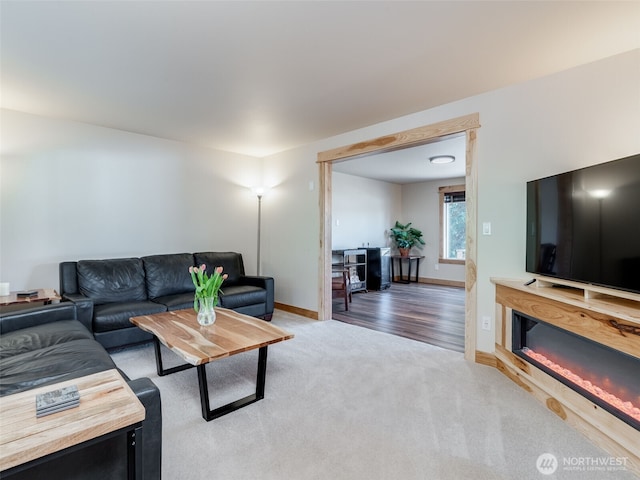 living area featuring a glass covered fireplace, light carpet, and baseboards