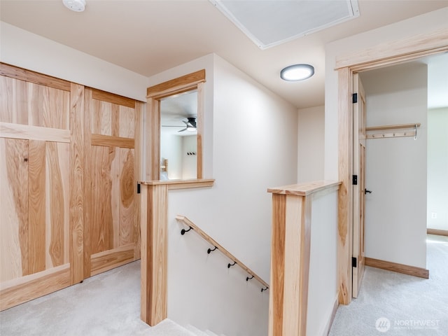 hallway with an upstairs landing, light colored carpet, and baseboards