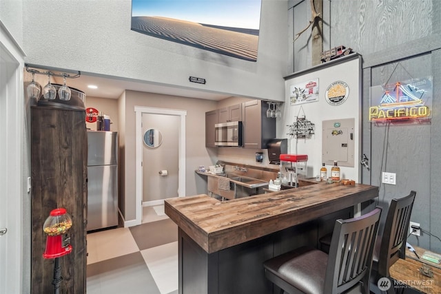 kitchen with appliances with stainless steel finishes, butcher block counters, a breakfast bar area, and a towering ceiling