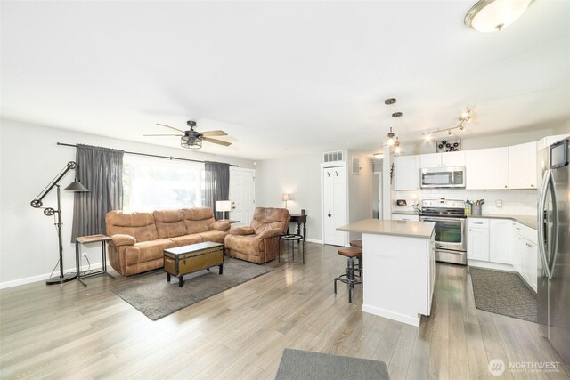 living room featuring a ceiling fan, baseboards, visible vents, and light wood finished floors