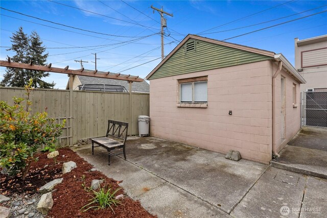 rear view of house with a patio, fence, and concrete block siding