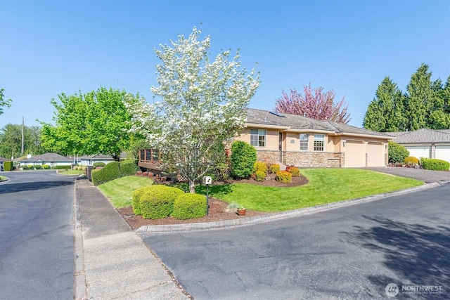 view of front of house featuring a front lawn, driveway, stone siding, and an attached garage
