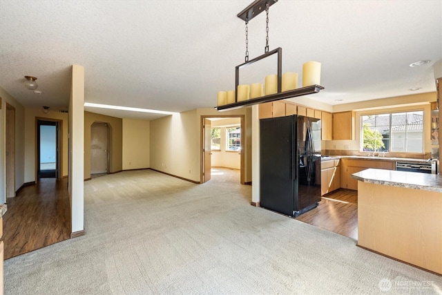 kitchen with light colored carpet, arched walkways, light brown cabinetry, dishwashing machine, and black fridge