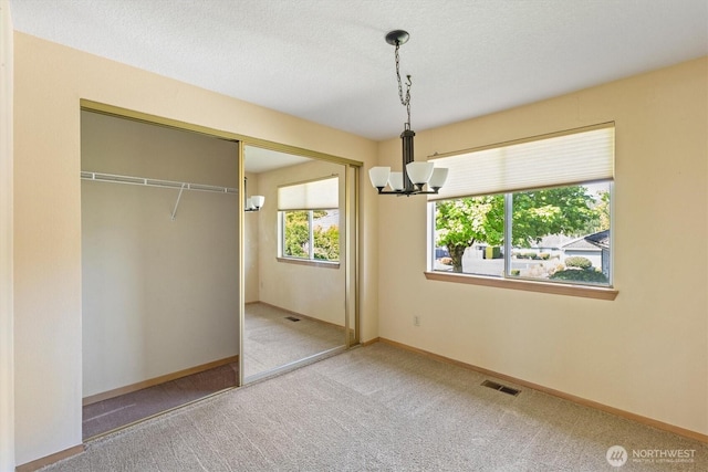 unfurnished bedroom with visible vents, a closet, baseboards, carpet floors, and a notable chandelier