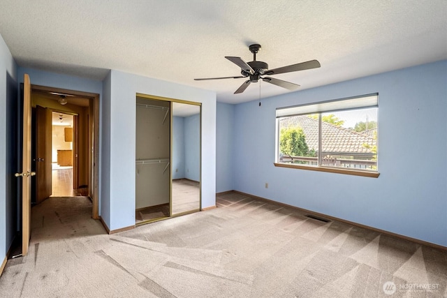unfurnished bedroom with a textured ceiling, carpet flooring, baseboards, a closet, and a ceiling fan