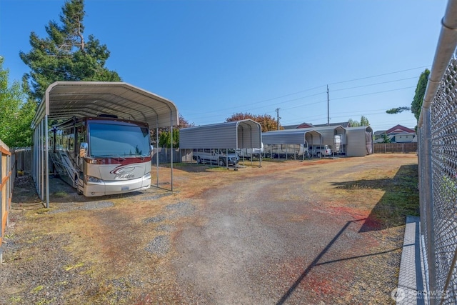 view of vehicle parking with a detached carport, dirt driveway, and fence