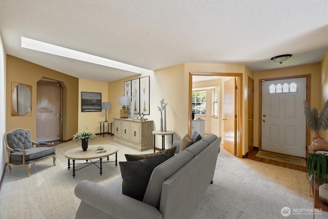 living room with baseboards, arched walkways, and light carpet