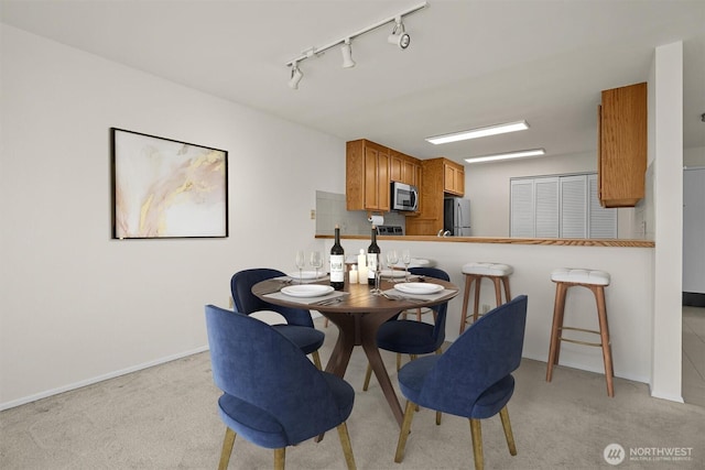 dining room with baseboards, light carpet, and rail lighting