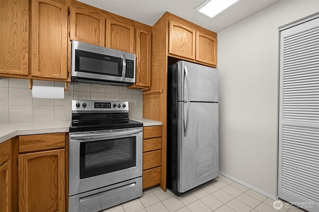 kitchen featuring brown cabinetry, light tile patterned flooring, light countertops, appliances with stainless steel finishes, and backsplash