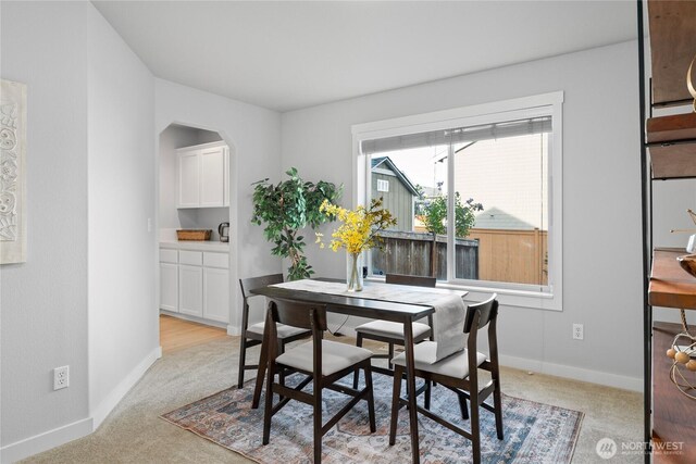 dining space with arched walkways, baseboards, and light carpet