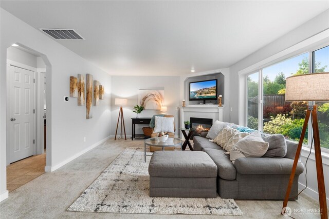 living room featuring baseboards, light colored carpet, a glass covered fireplace, and visible vents