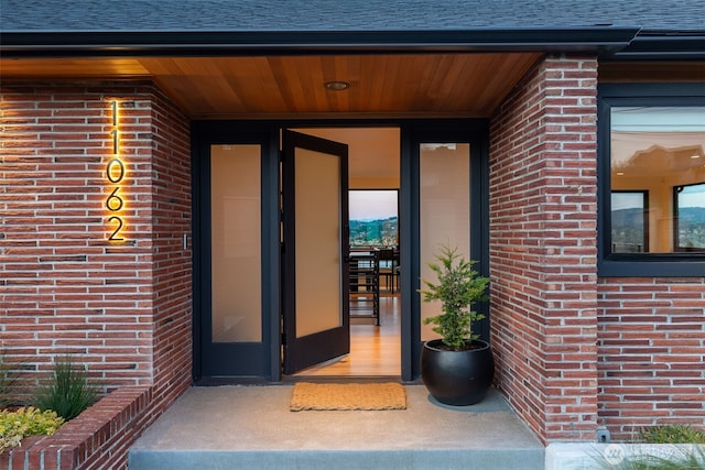 property entrance featuring brick siding and roof with shingles