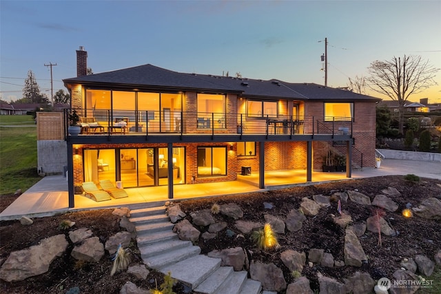 back of house at dusk with brick siding, a chimney, and a patio