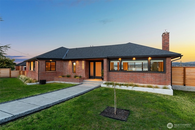 view of front of house featuring fence, a chimney, a front yard, and brick siding