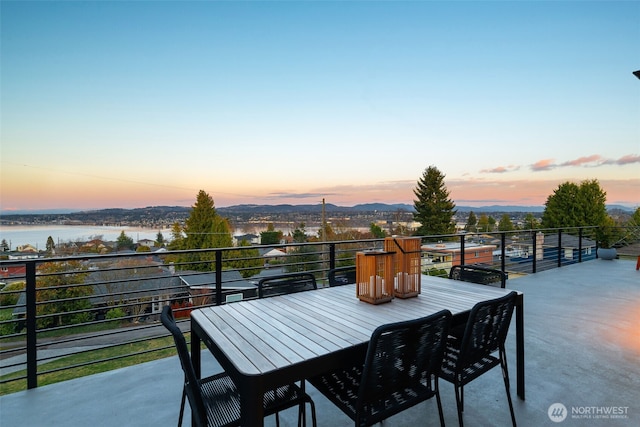 balcony at dusk featuring outdoor dining space and a water view
