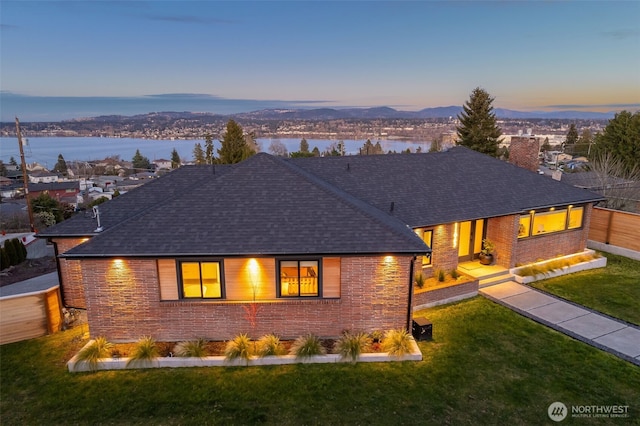 ranch-style home featuring brick siding, fence, a front lawn, and roof with shingles