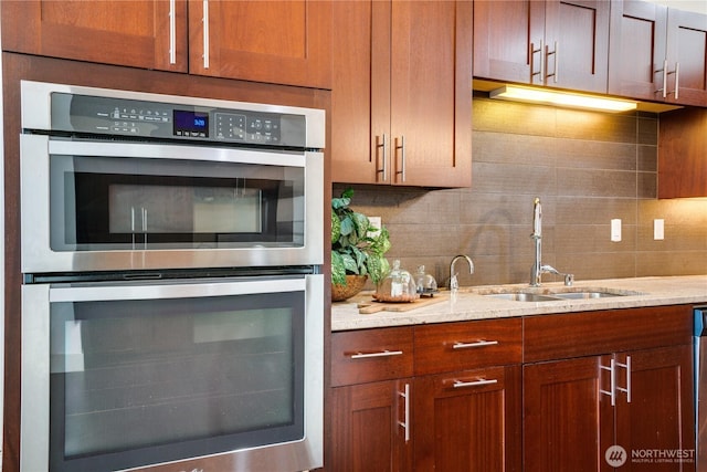 kitchen featuring light stone countertops, a sink, brown cabinetry, stainless steel appliances, and backsplash