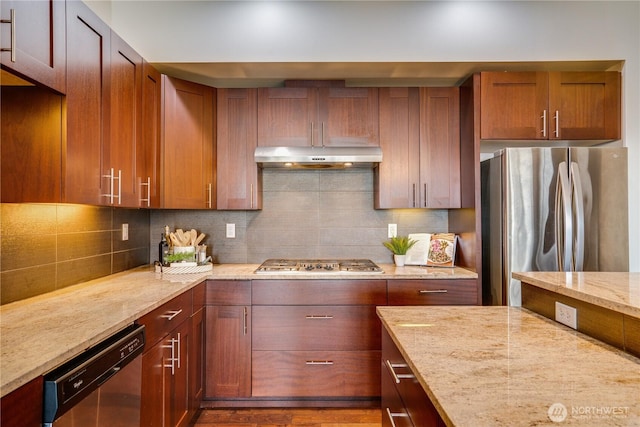 kitchen featuring light stone counters, appliances with stainless steel finishes, under cabinet range hood, and tasteful backsplash