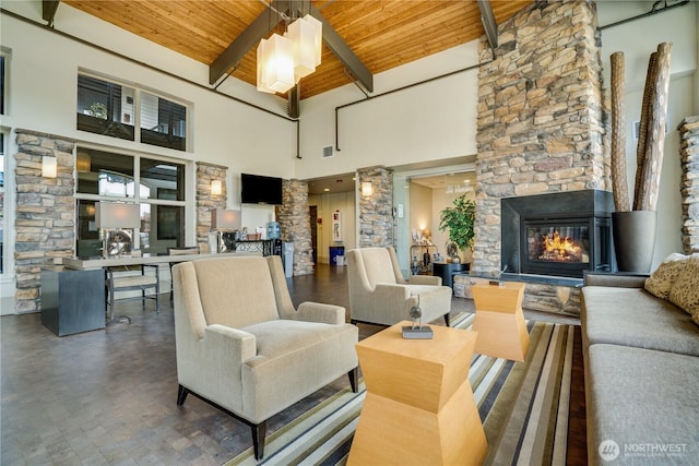living room with beam ceiling, wooden ceiling, a glass covered fireplace, a high ceiling, and ornate columns