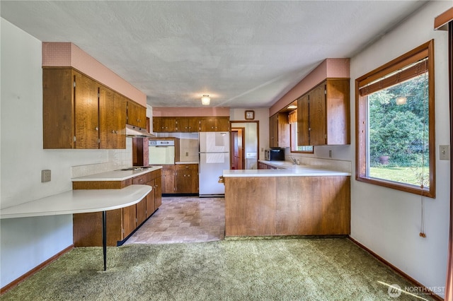 3828 Harbel Dr NE, Bremerton, WA 98310 - kitchen with white appliances, light countertops, under cabinet range hood, a peninsula, and brown cabinetry